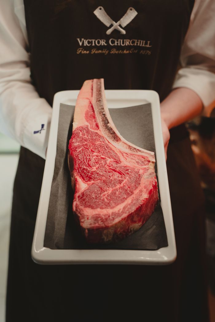 services-03 Close-up of butcher presenting a marbled beef steak on a tray, ready for cooking.