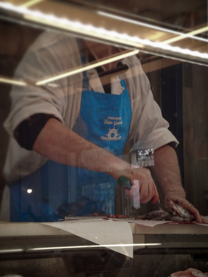 get-in-touch Fishmonger slicing fresh fish indoors with visible reflections on the glass counter.