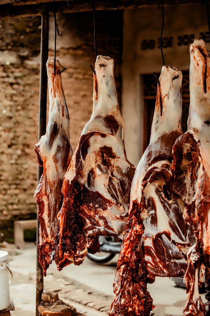 Close-up of butchered animal carcasses hanging in an outdoor market setting.