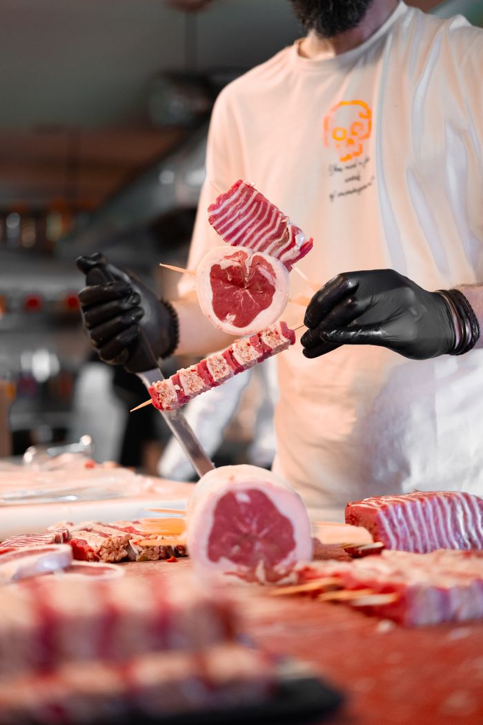 who-we-are Butcher arranging raw meat skewers with precision in a modern kitchen setup.