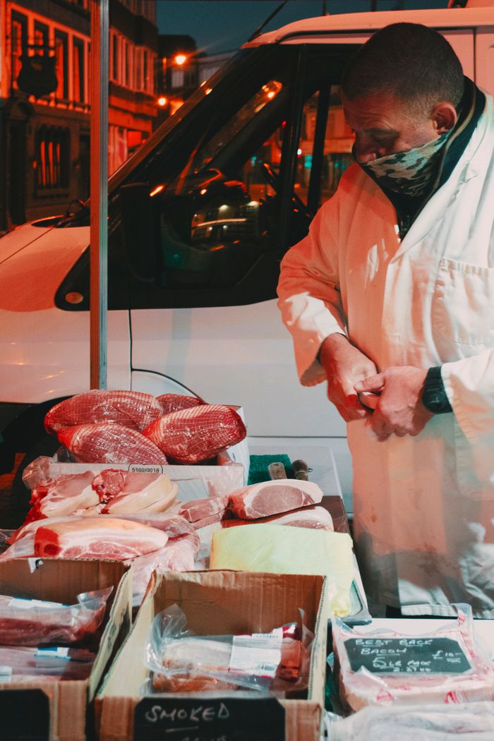 services-bg Street vendor sells fresh meats at an outdoor night market, showcasing various cuts.